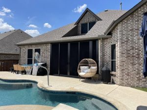 Multi-panel black sliding security screen patio enclosure next to residential swimming pool in Dallas TX by Security Screen Masters of Texas