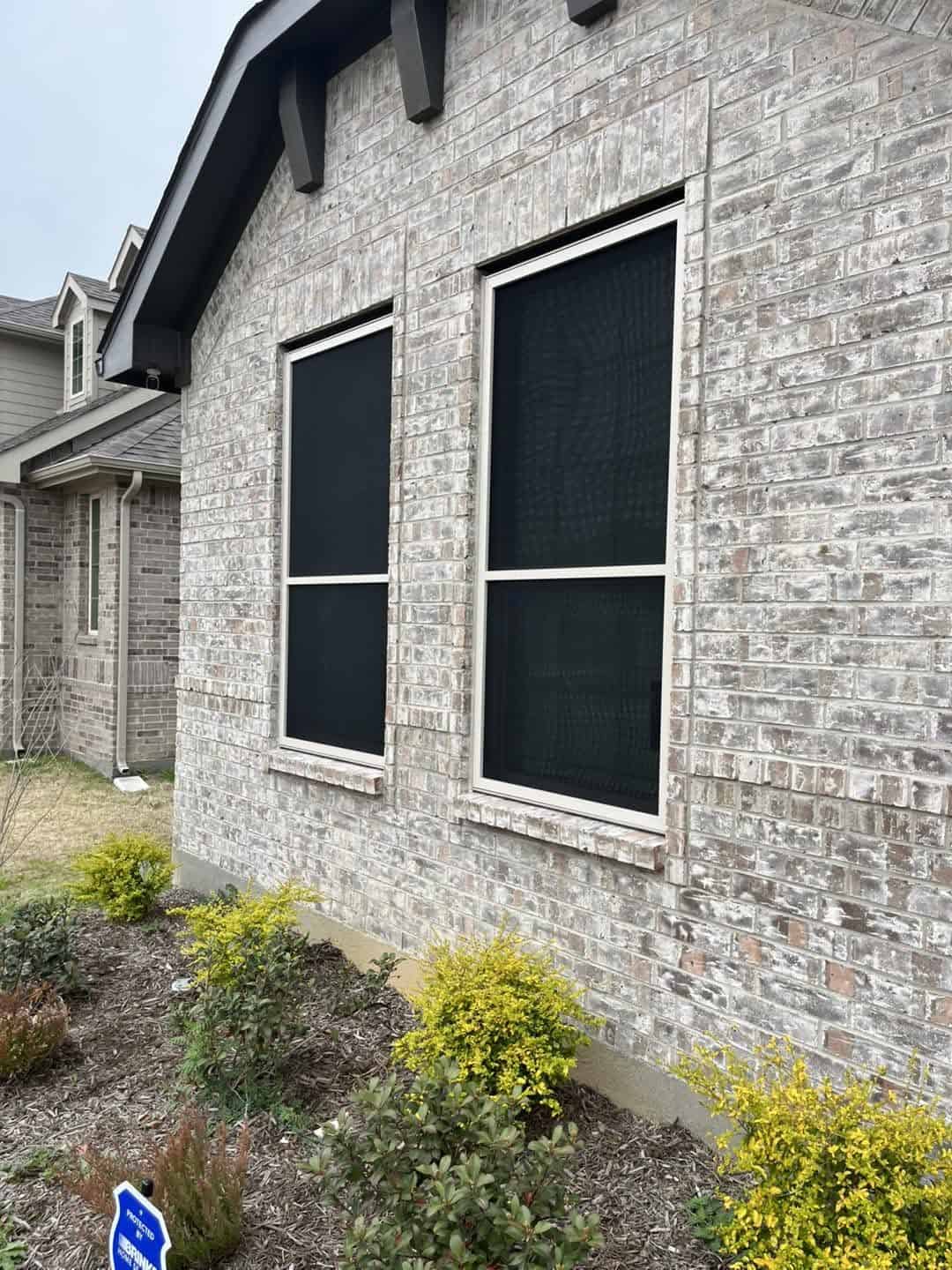 Double-hung security window screens on whitewashed brick home in Grapevine TX by Security Screen Masters of Texas