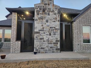 Outdoor living space security screen doors installed around stone fireplace by Security Screen Masters of Texas