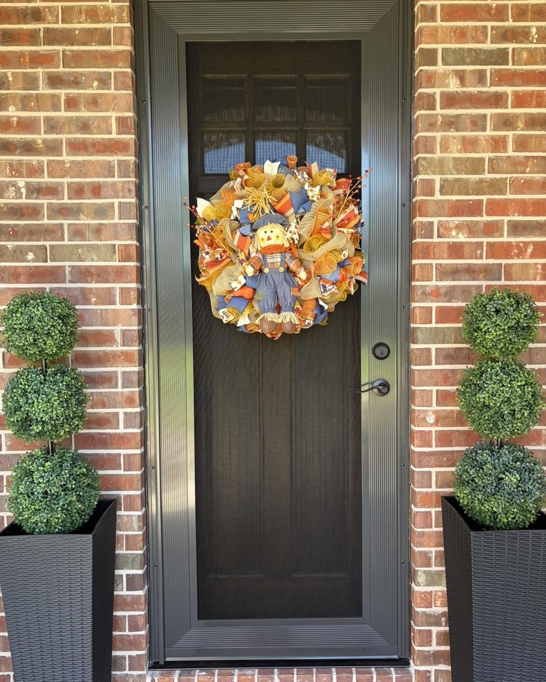 Bronze front entry security screen door with autumn wreath on brick home by Security Screen Masters of Texas